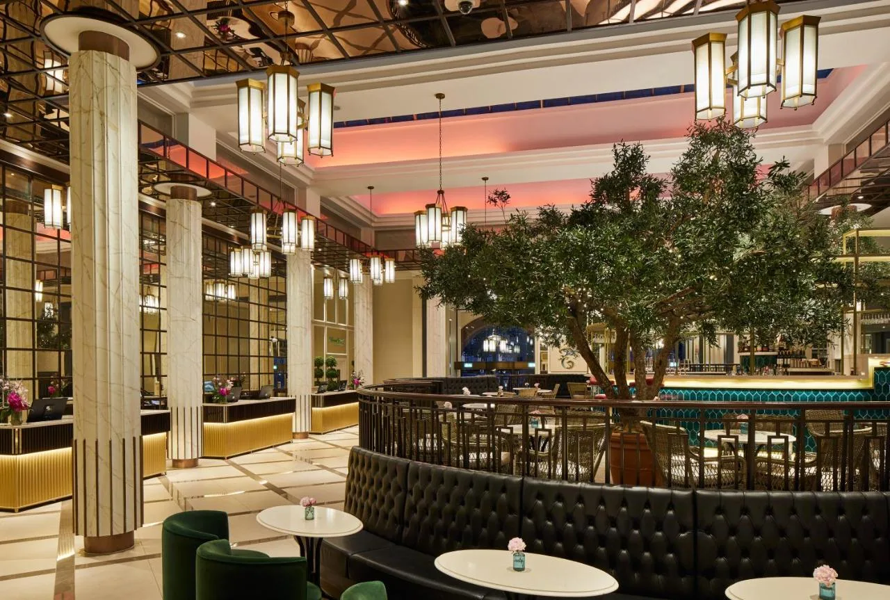 a large lobby with tables and a tree in the middle at The Midland in Manchester